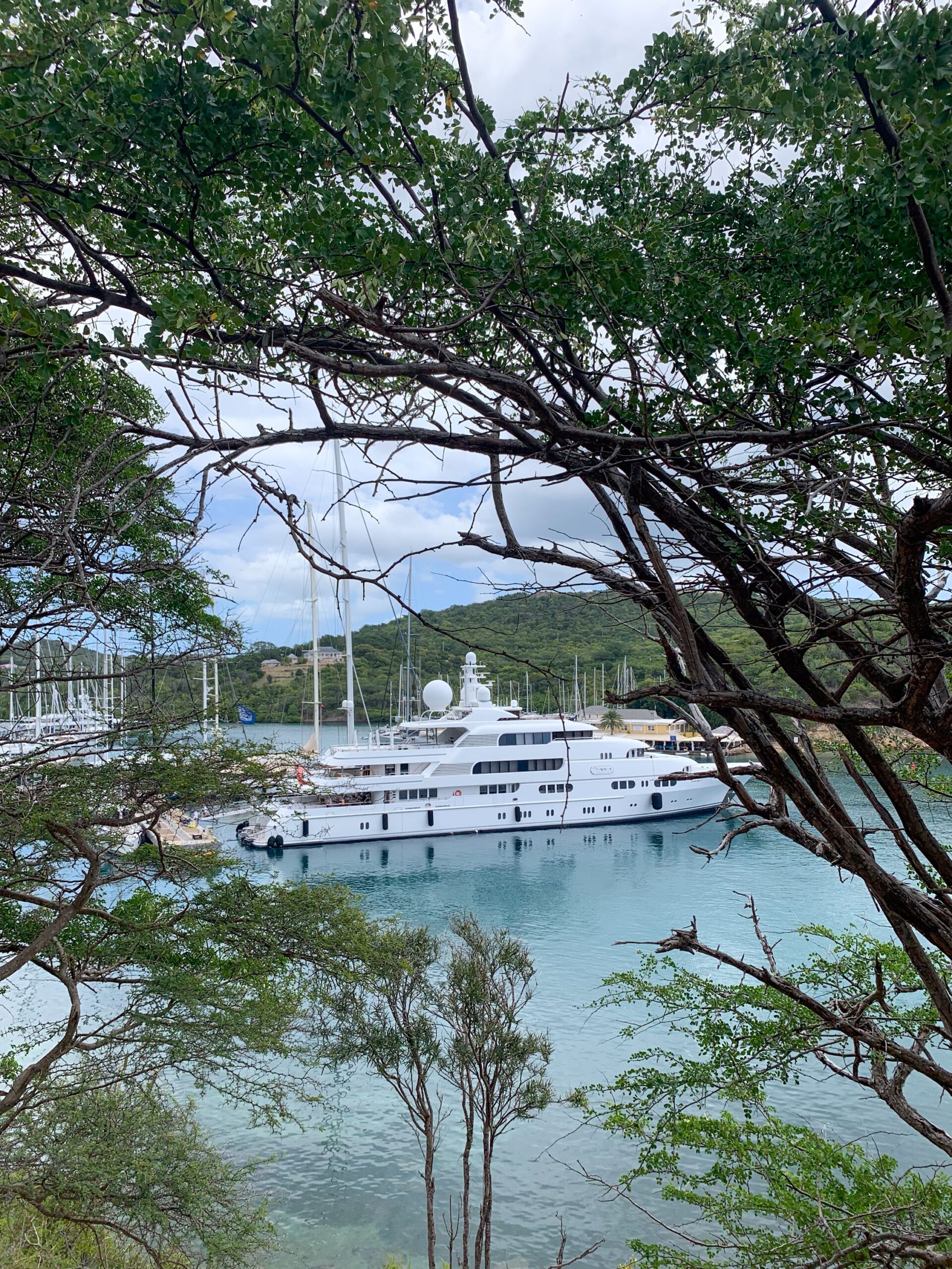 A yacht moored in English Harbour, Antigua, surrounded by tropical trees and calm blue water