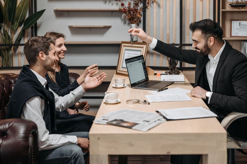 A real estate professional handing house keys to smiling clients at a desk
