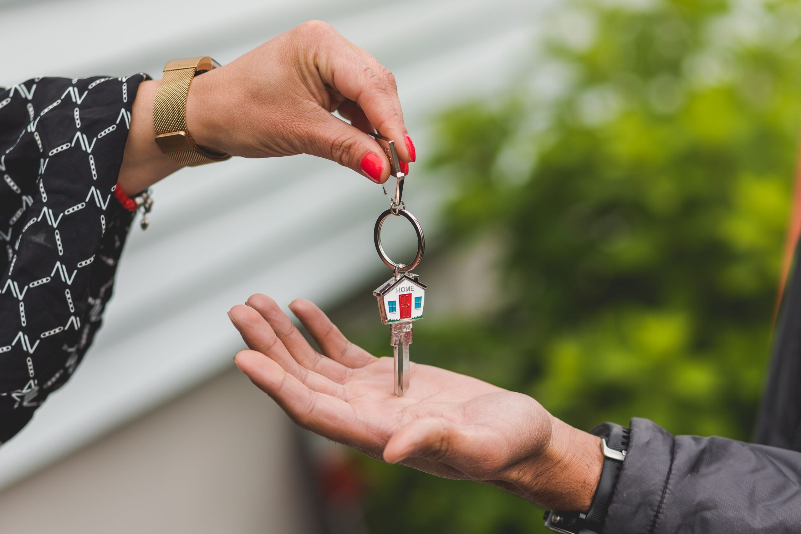 Close-up of a hand handing over a house key with a house-shaped keychain, symbolizing a real estate transaction